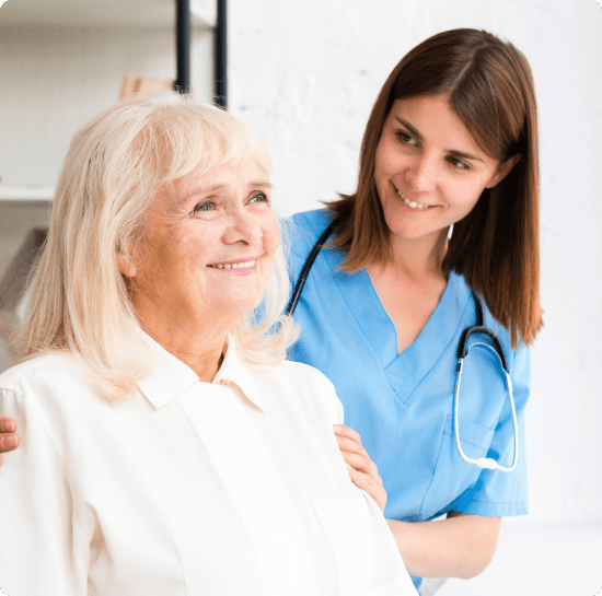 best-friends-approach A nurse with a stethoscope smiles behind an elderly woman in white, who gazes away contentedly against a blurred white wall.