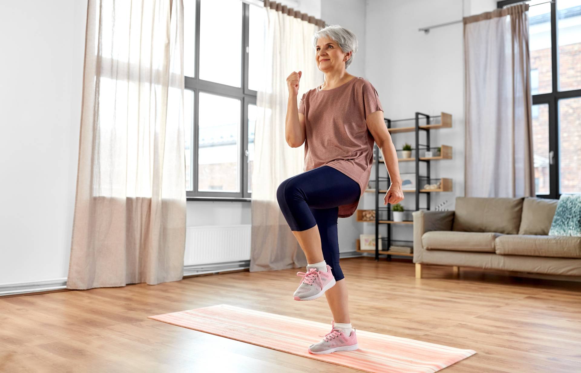 Old woman doing standing marches in her living room.