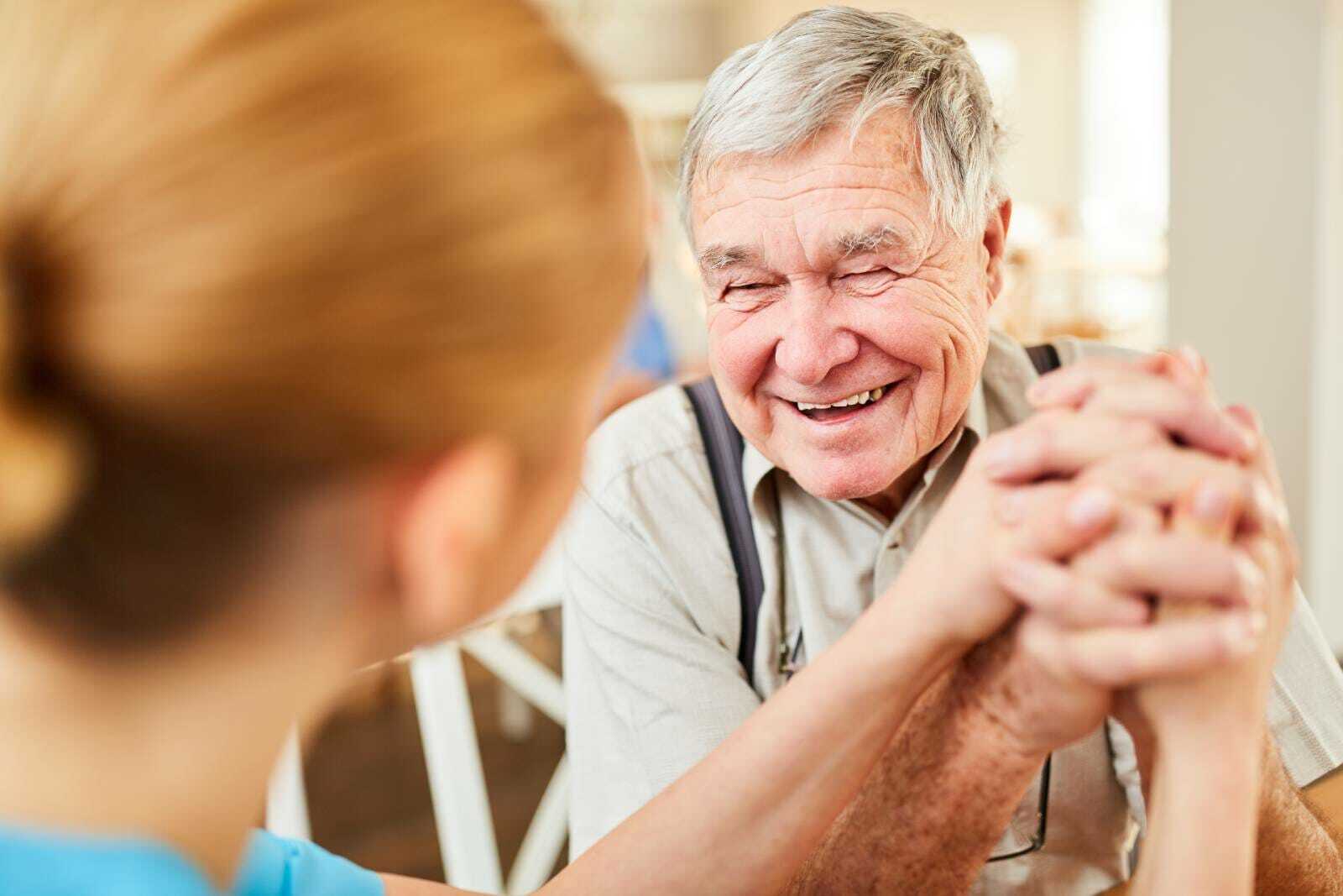 Senior man with dementia smiling while engaging in conversation with another person.