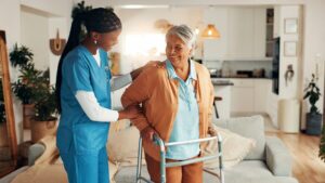 Caregiver supporting an older woman using a walker at home.