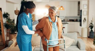 Caregiver supporting an older woman using a walker at home.