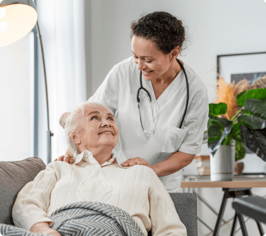 Elderly woman receiving dementia support from her woman caregiver in her living room.