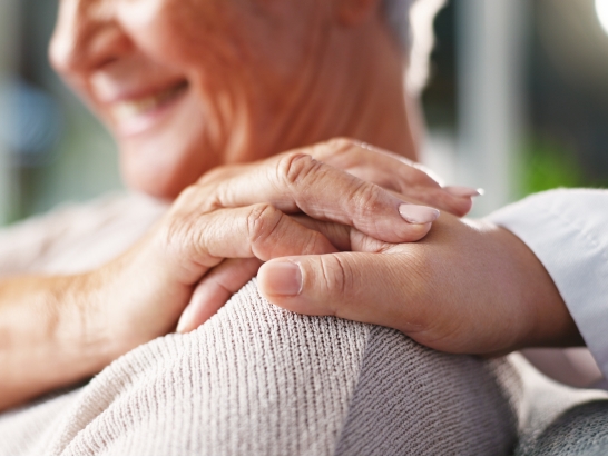 Honest About Privacy-image Close-up of a caregiver's hand resting on the shoulder of a smiling elderly man