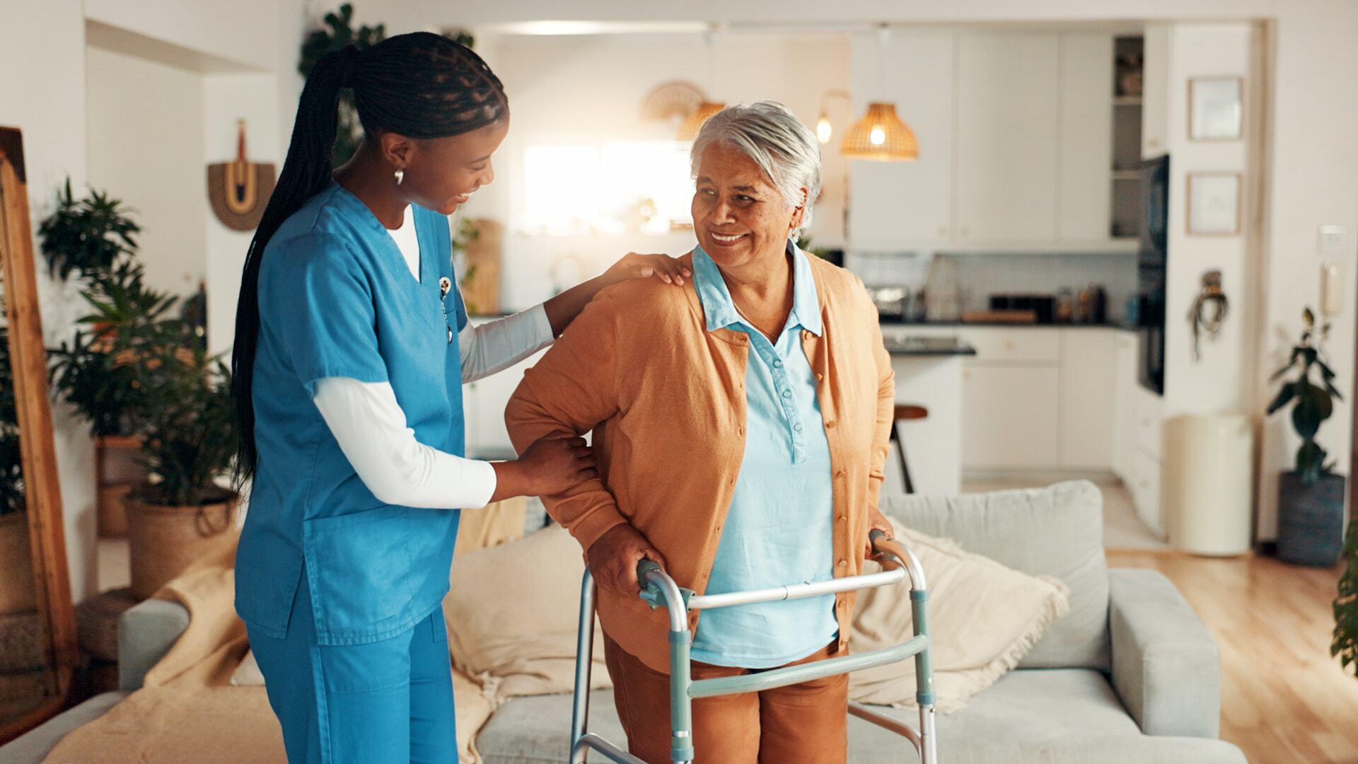 Caregiver supporting an older woman using a walker at home.