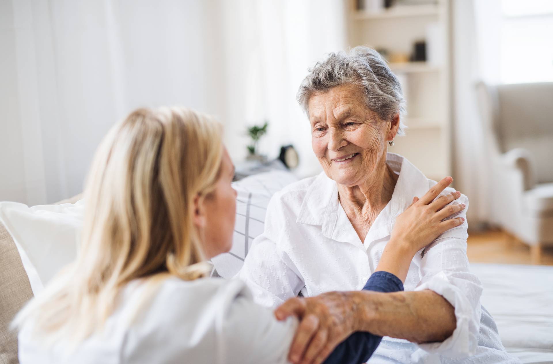 Smiling elderly woman sitting at home with a caregiver offering support