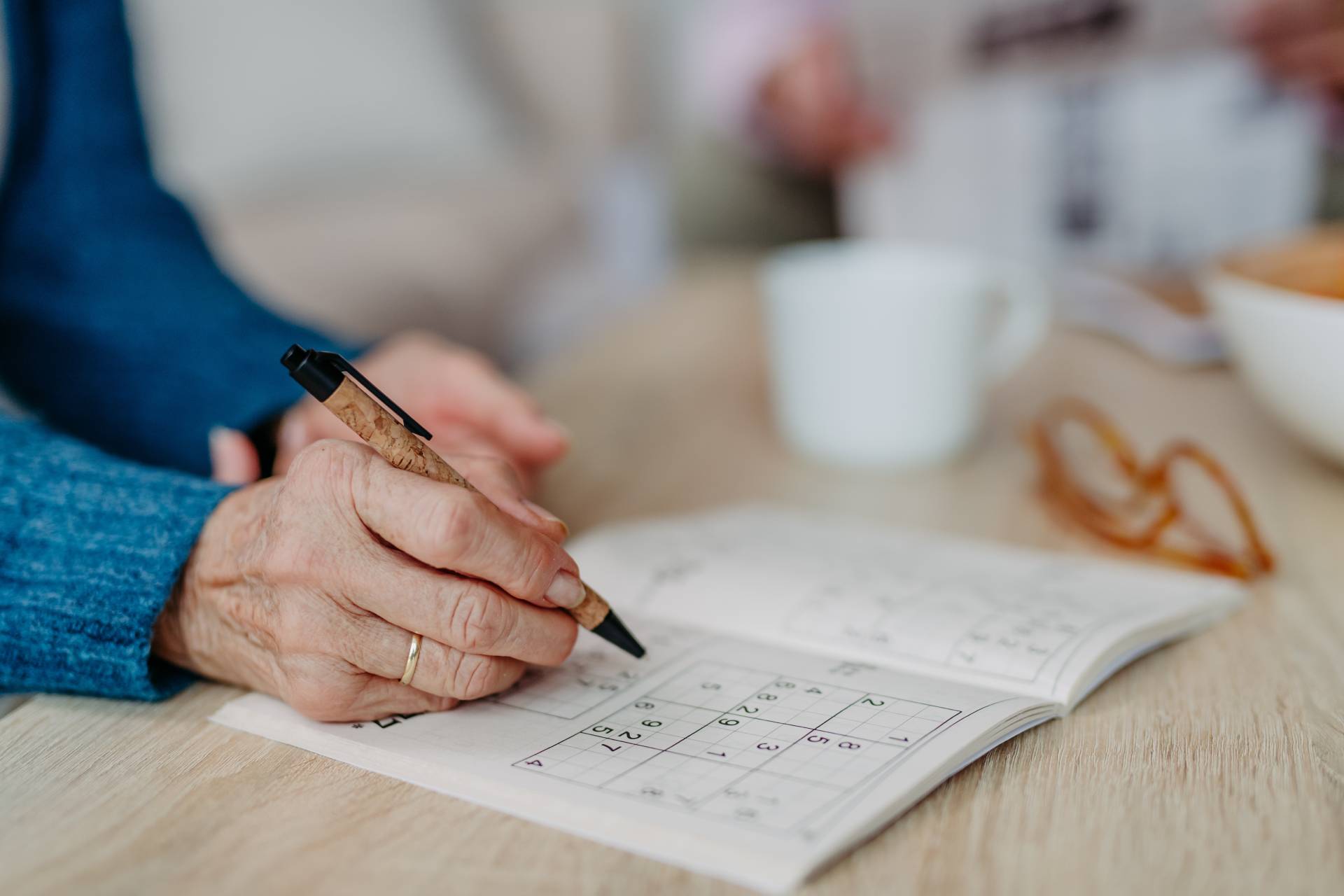 A senior solving a sudoku number puzzle at a table