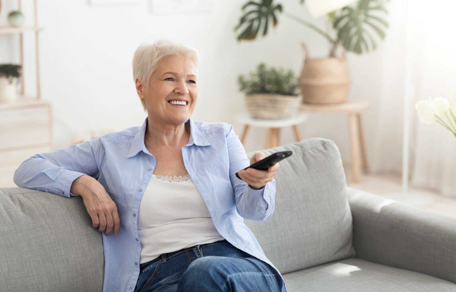 Senior woman smiling while holding a remote about to watch a movie.