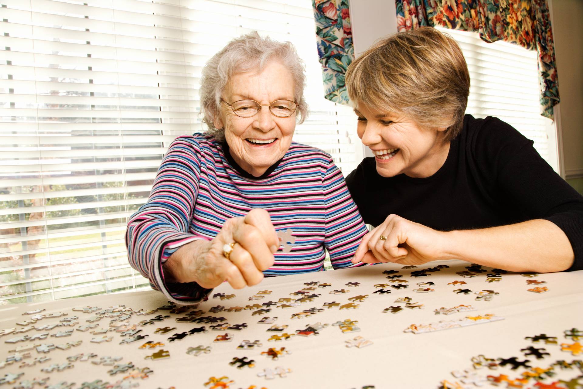 A senior and her caregiver working on a jigsaw puzzle together