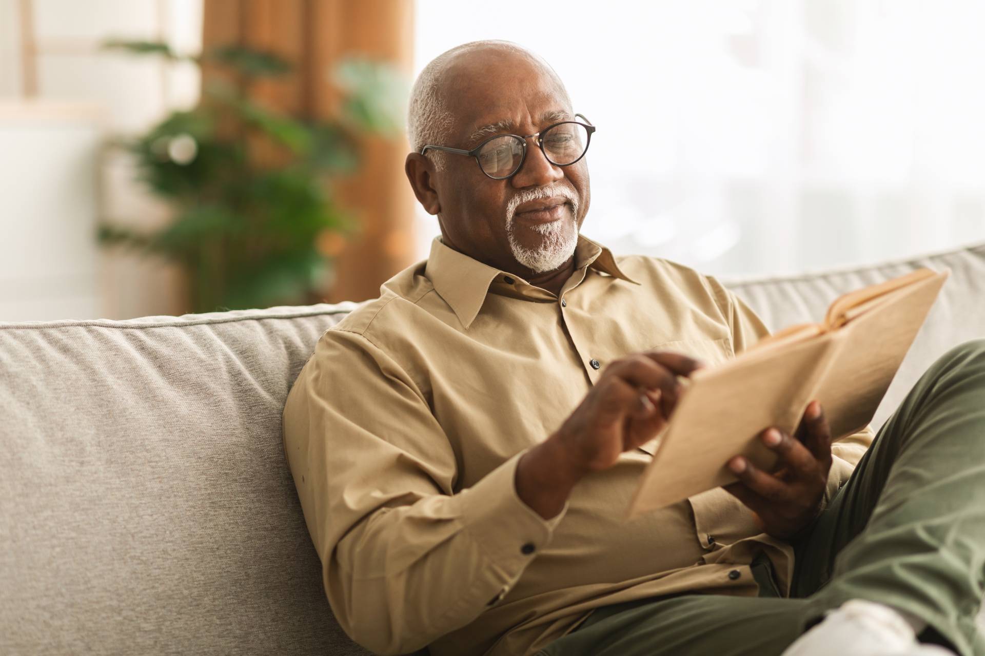 An elderly man enjoying reading a book on his couch