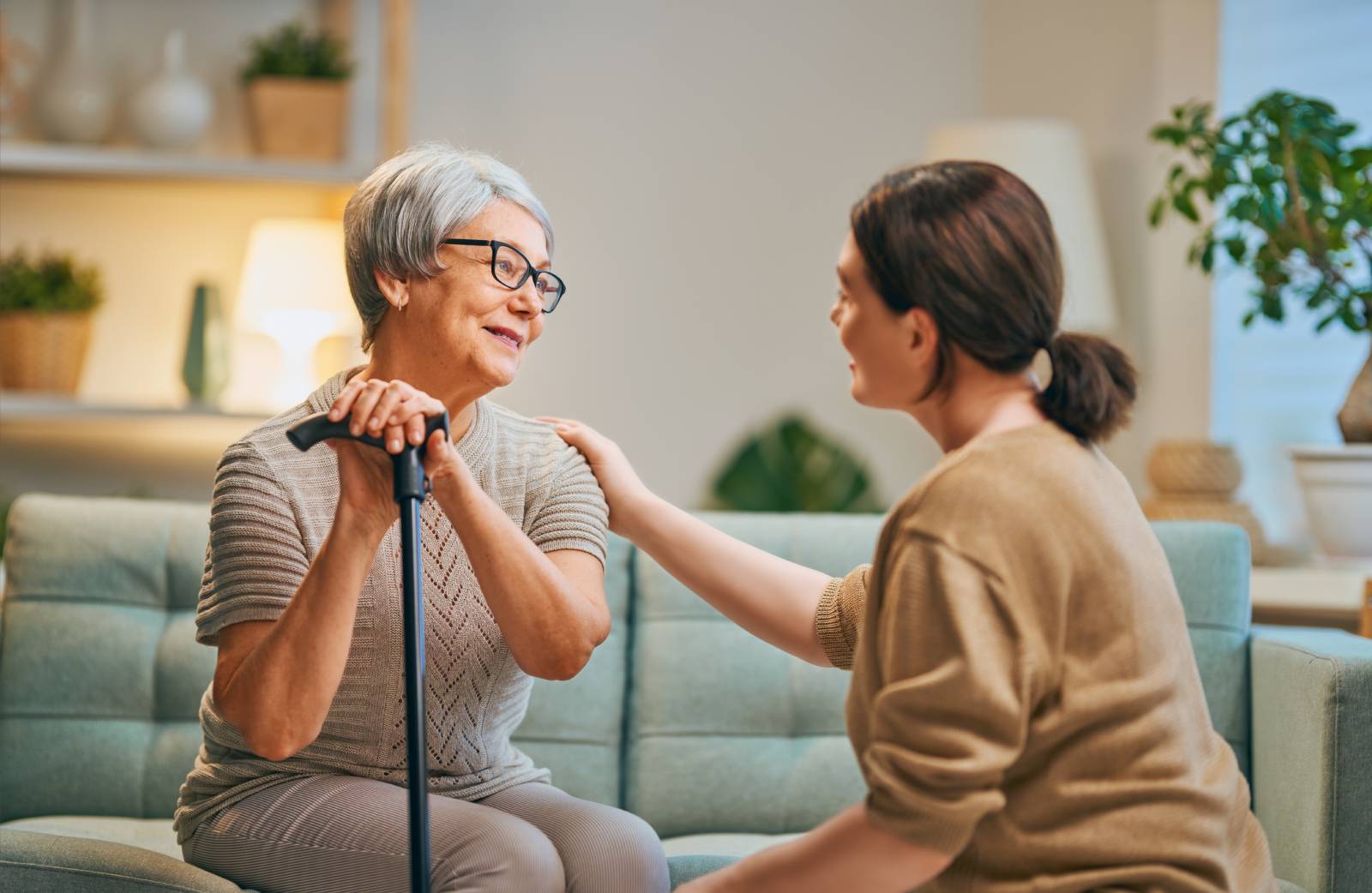 A senior sitting on a couch talking to a caregiver.