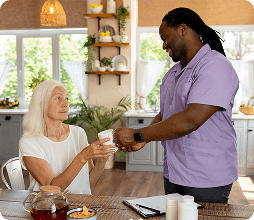 Elderly woman grabbing a cup from a palliative home care caregiver.