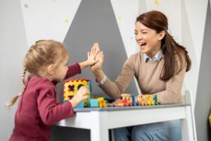 Adult and young child playing with colourful learning toys at a table and giving a high-five during an early childhood learning activity.