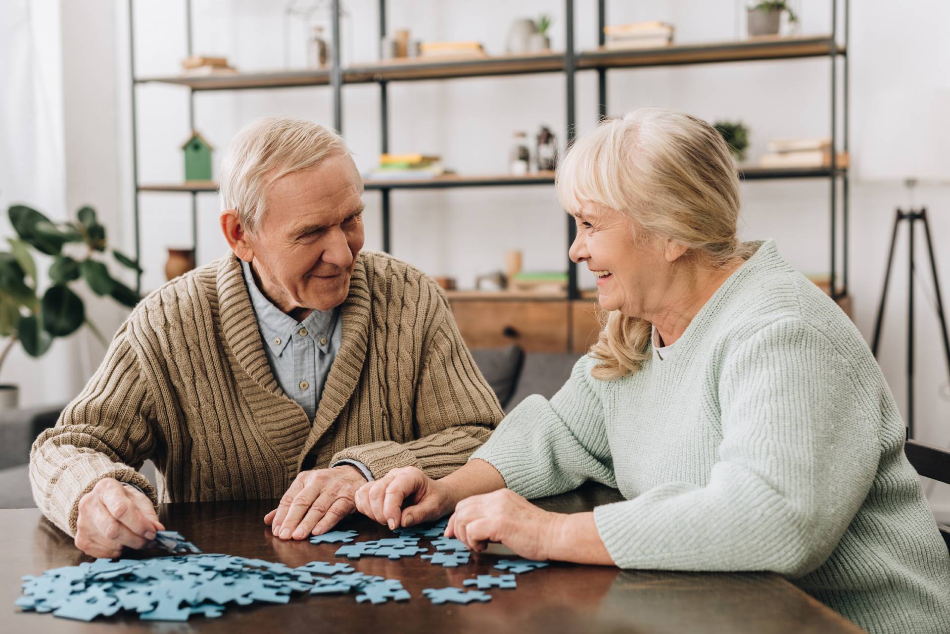 An older couple smiling and working together on a puzzle at a table.
