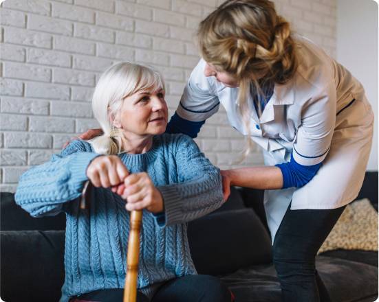 Caregiver assisting an elderly woman with a cane in her living room