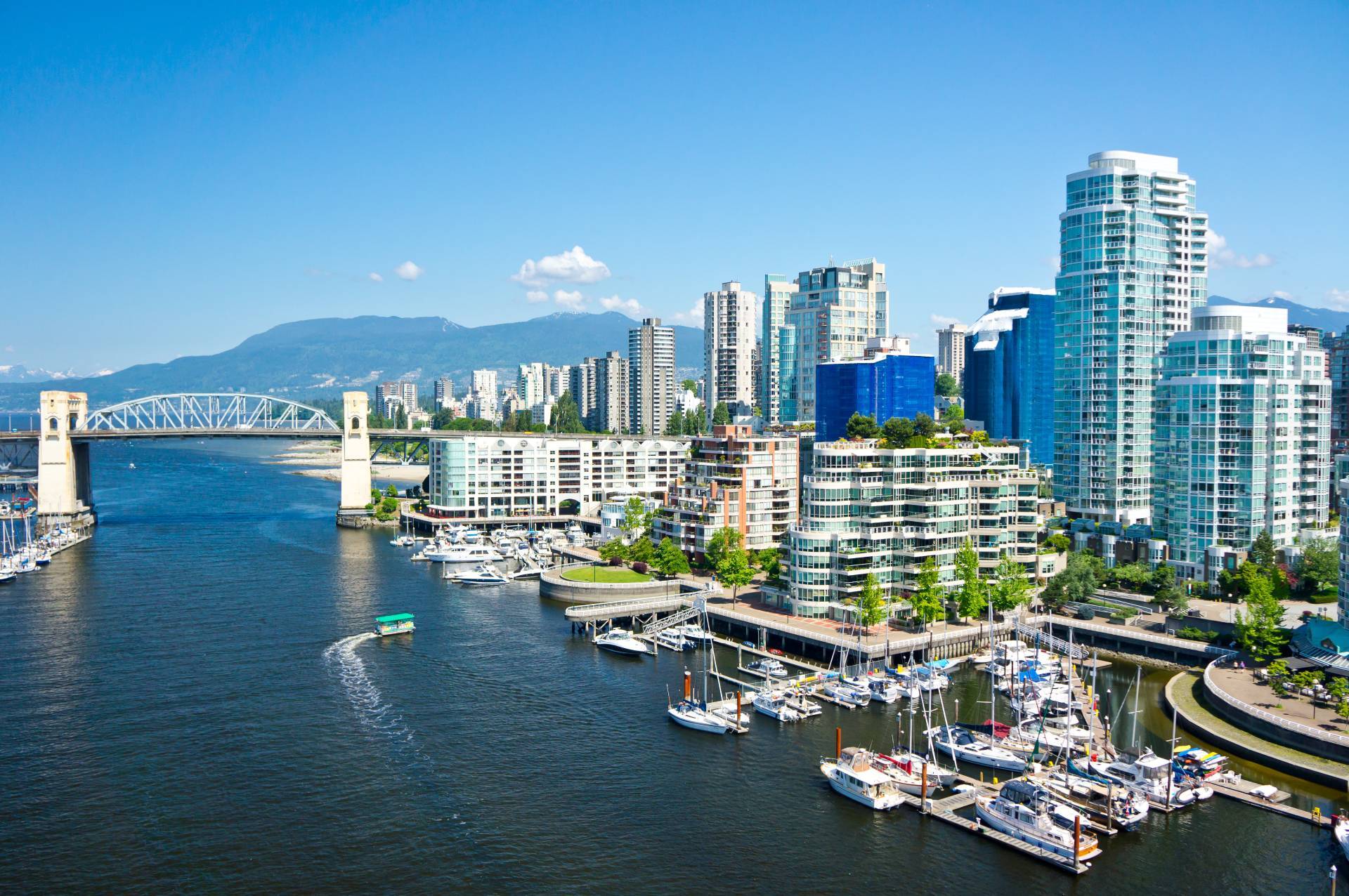 Vancouver False Creek waterfront with the Burrard Street Bridge, downtown high-rises, marina boats, and the North Shore mountains in the background