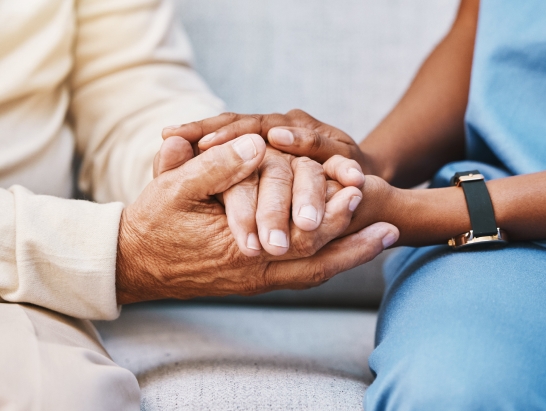 Close-up of an elderly man's hands being held by a caregiver's hands
