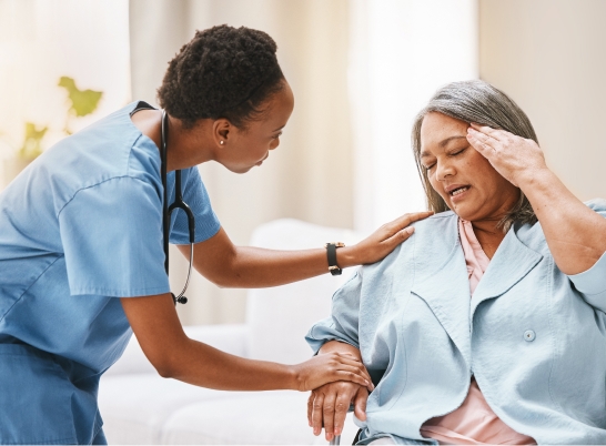 Caregiver comforting an elderly woman who is holding her head in discomfort