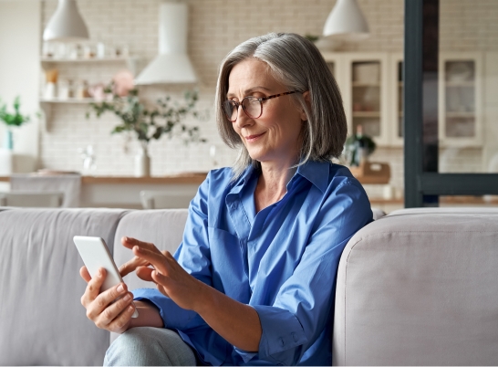 Older woman sitting on a couch checking her smartphone