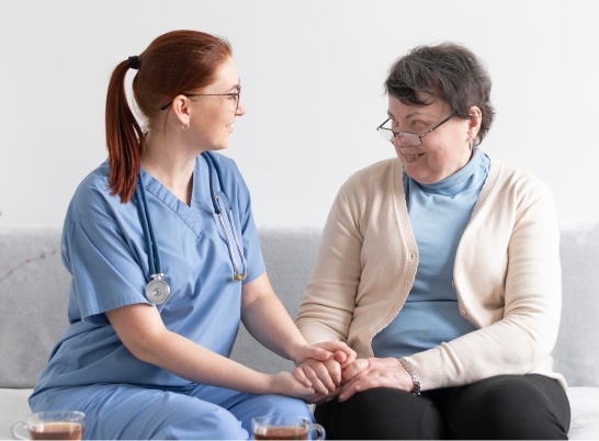 Caregiver holding hands with an elderly woman while talking on a couch