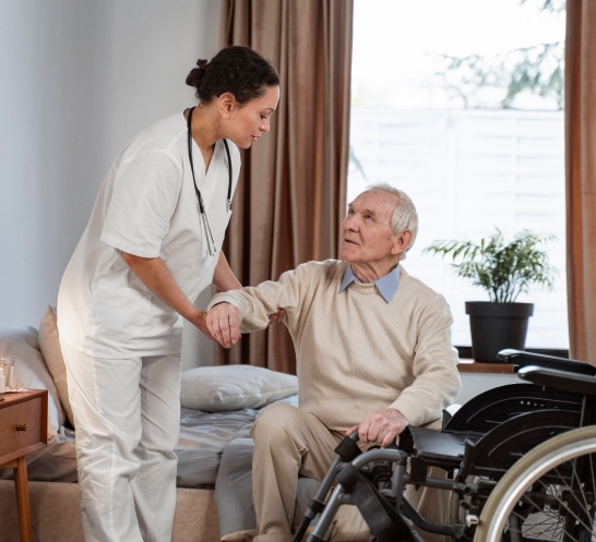 Caregiver helping an elderly man stand up beside his wheelchair