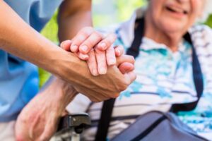 A caregiver holding the hand of an elderly woman