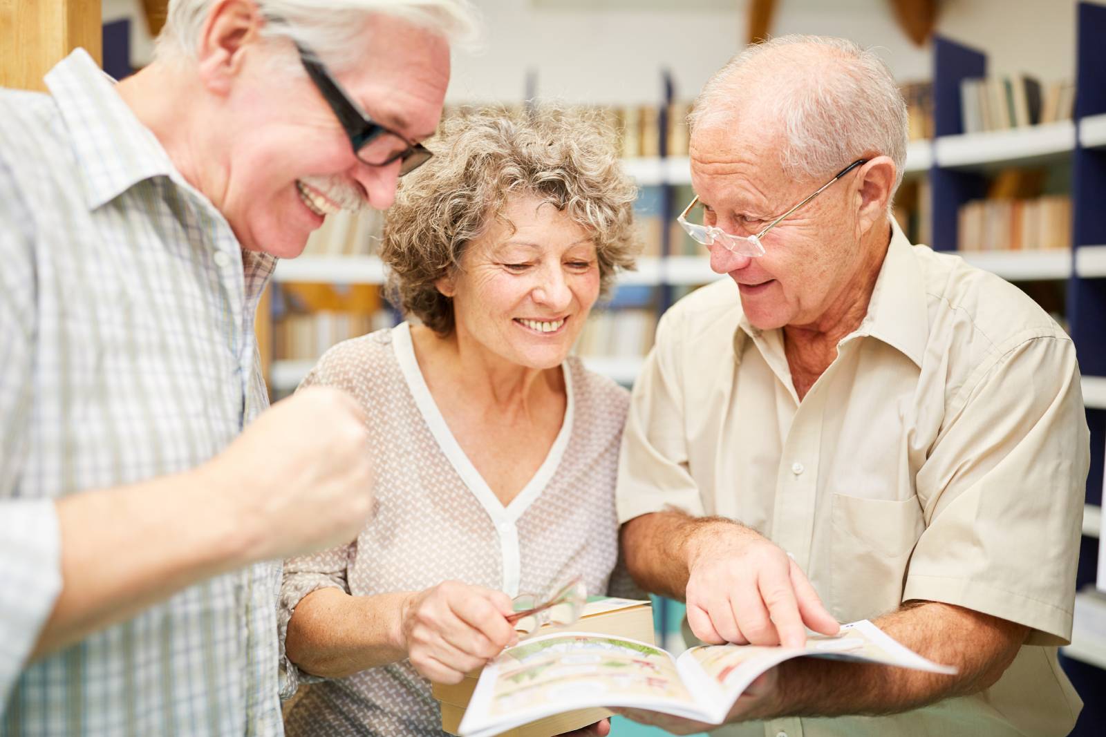 Three seniors reading in a library laughing.