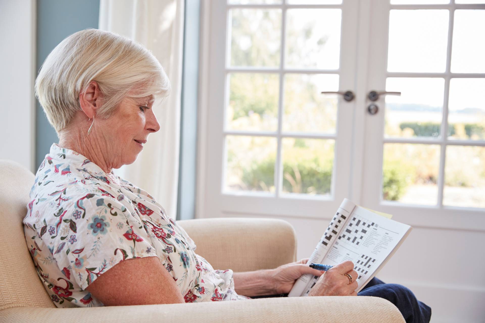 An elderly woman doing crossword puzzles in an armchair